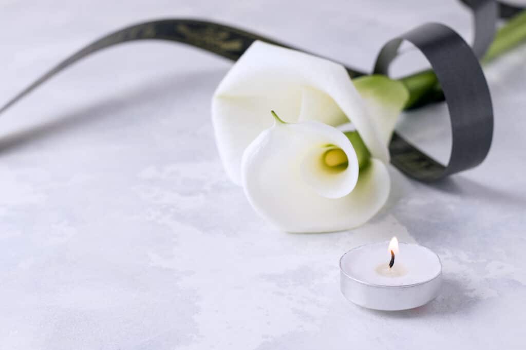 Weiße Calla mit schwarzem Trauerband und Teelicht – Symbolbild für Trauer und Abschied