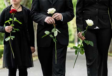 Vier Personen in dunkler Kleidung mit weißen Rosen