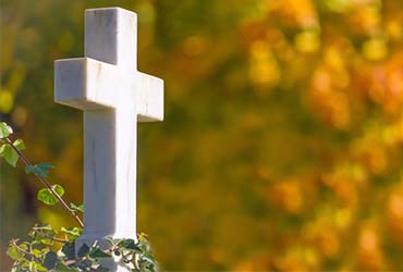 Weißes Kreuz vor herbstlich gefärbten Bäumen